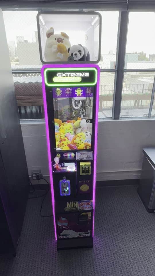A purple-lit claw machine in a lounge, tilting up from the cabinet to the plush on top