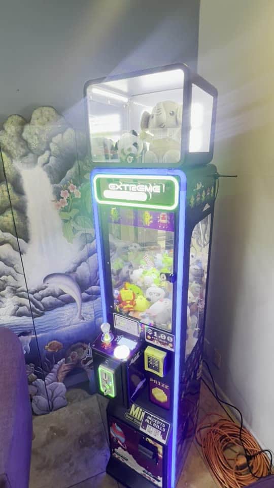A blue-lit California Claw machine in front of a waterfall mural