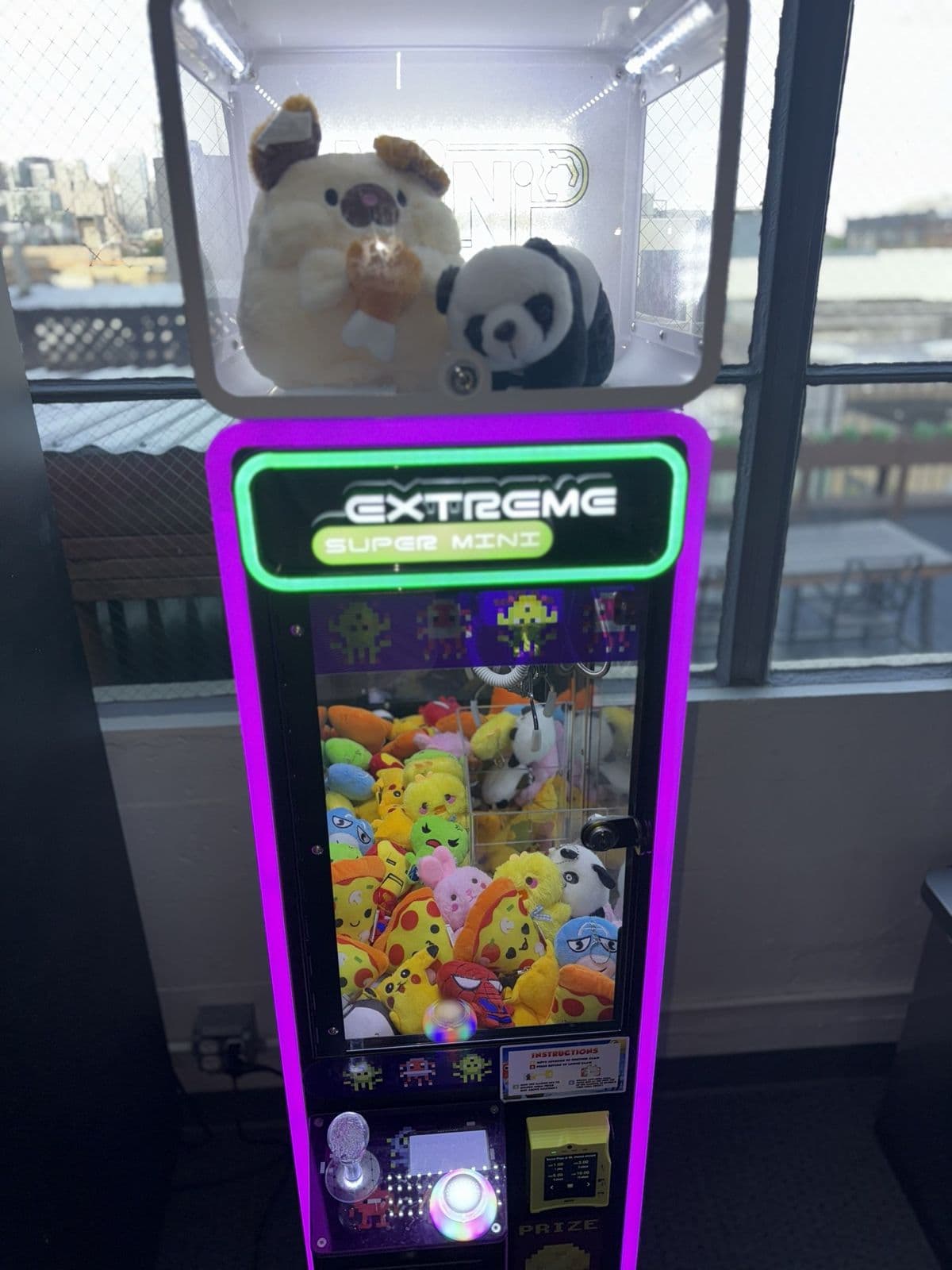 A purple-lit California Claw machine beside a tall window with a city view
