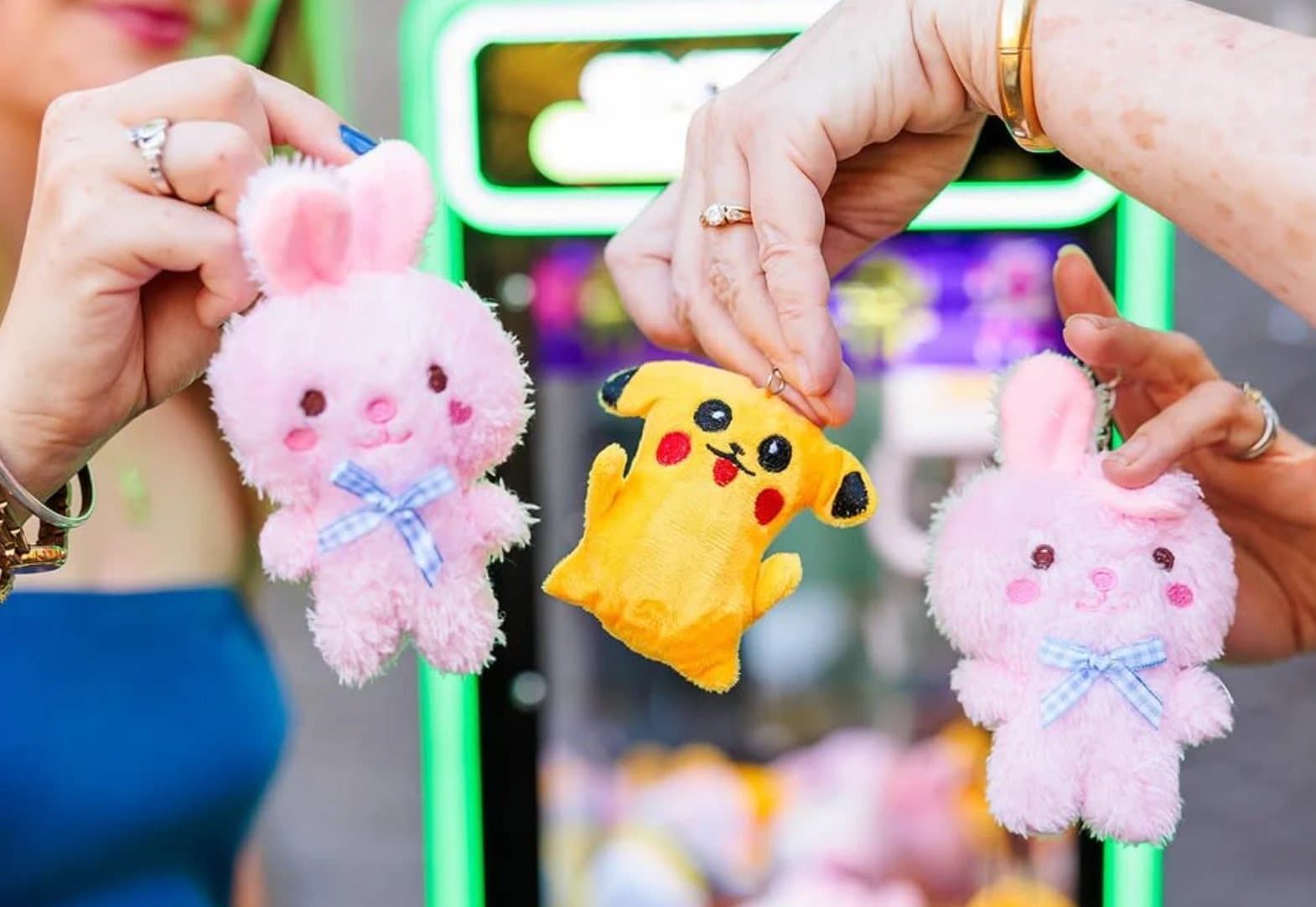 Three guests at an event holding plushies they won from a California Claw machine — two pink bunnies and a Pikachu